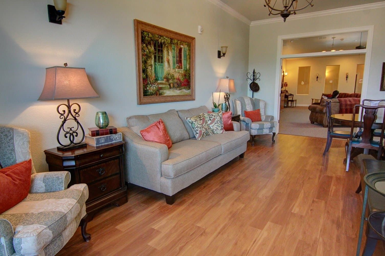A living room with a couch , chairs , lamps and a painting on the wall.