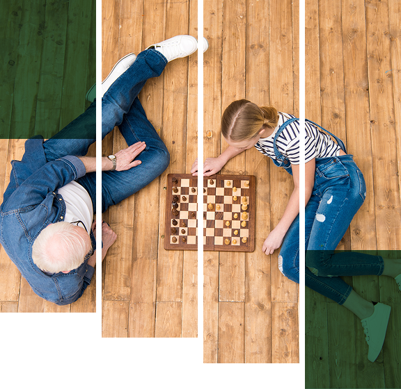 Two people playing chess on a wooden floor, viewed from above.