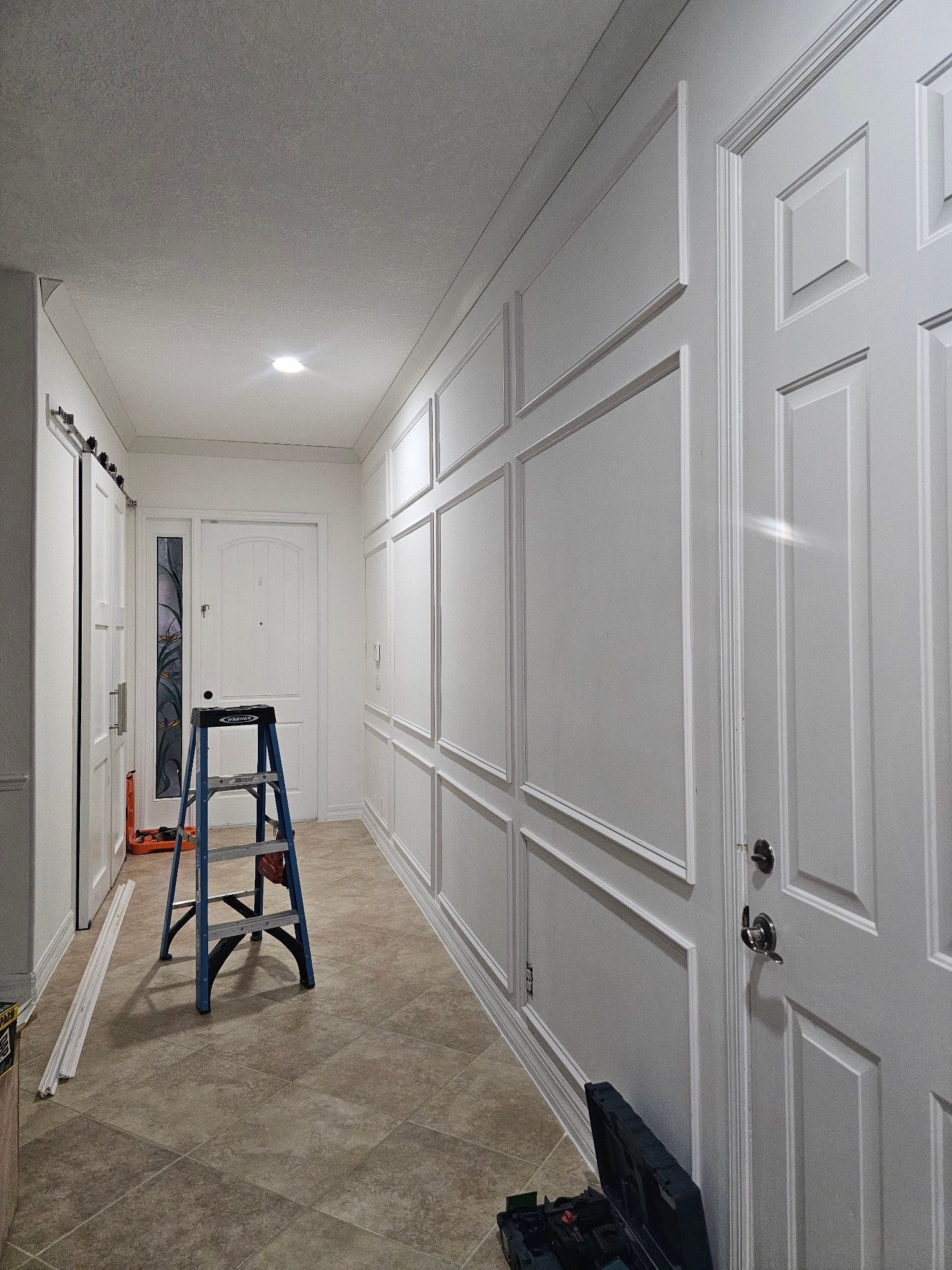 Hallway with white wainscoting and door trim. A blue stepladder sits near the center.