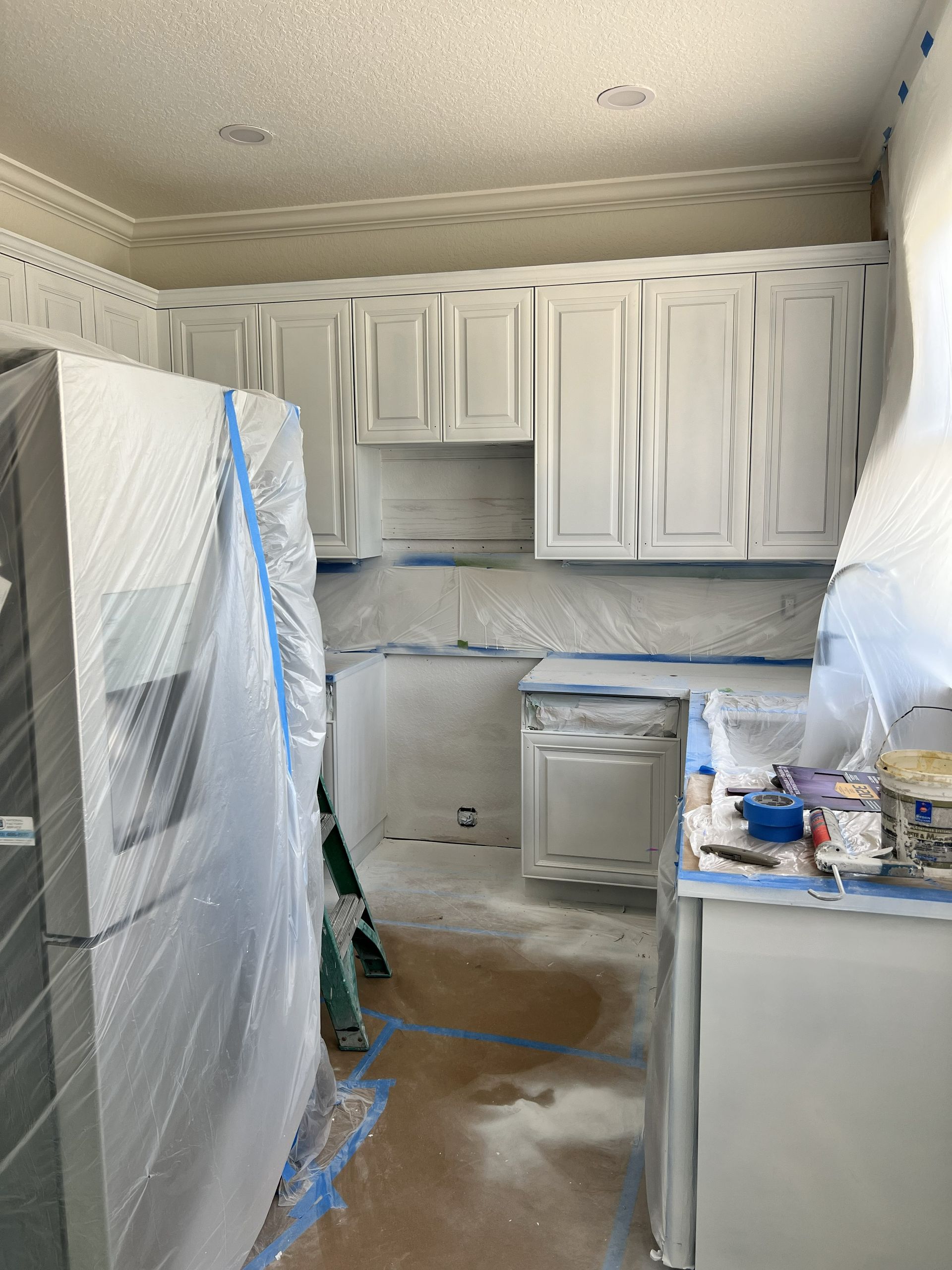Hand holding a paint roller applying white paint to a pale blue wall.