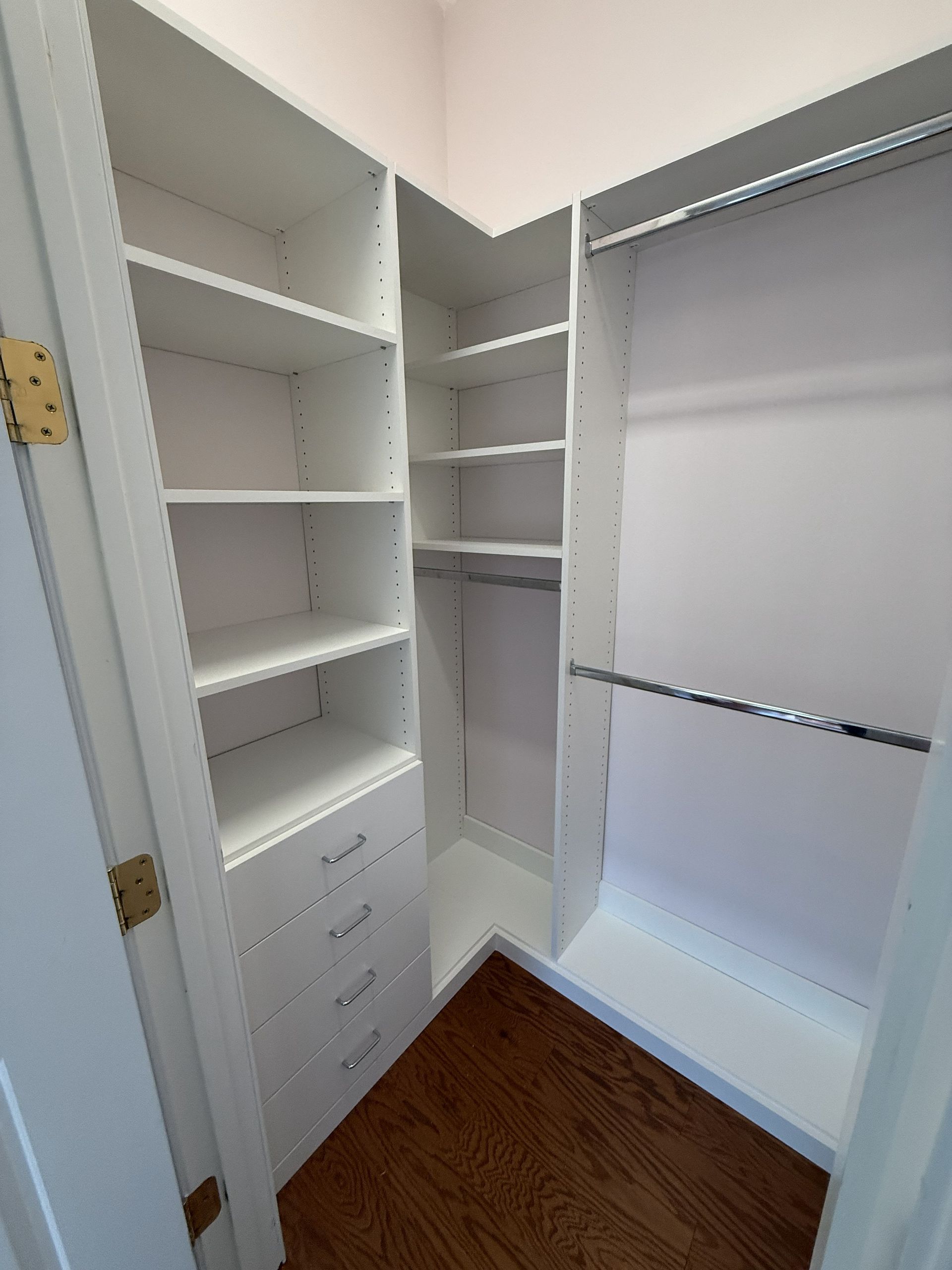 White walk-in closet with shelves, drawers, and hanging rods. Brown hardwood floor and pink walls.