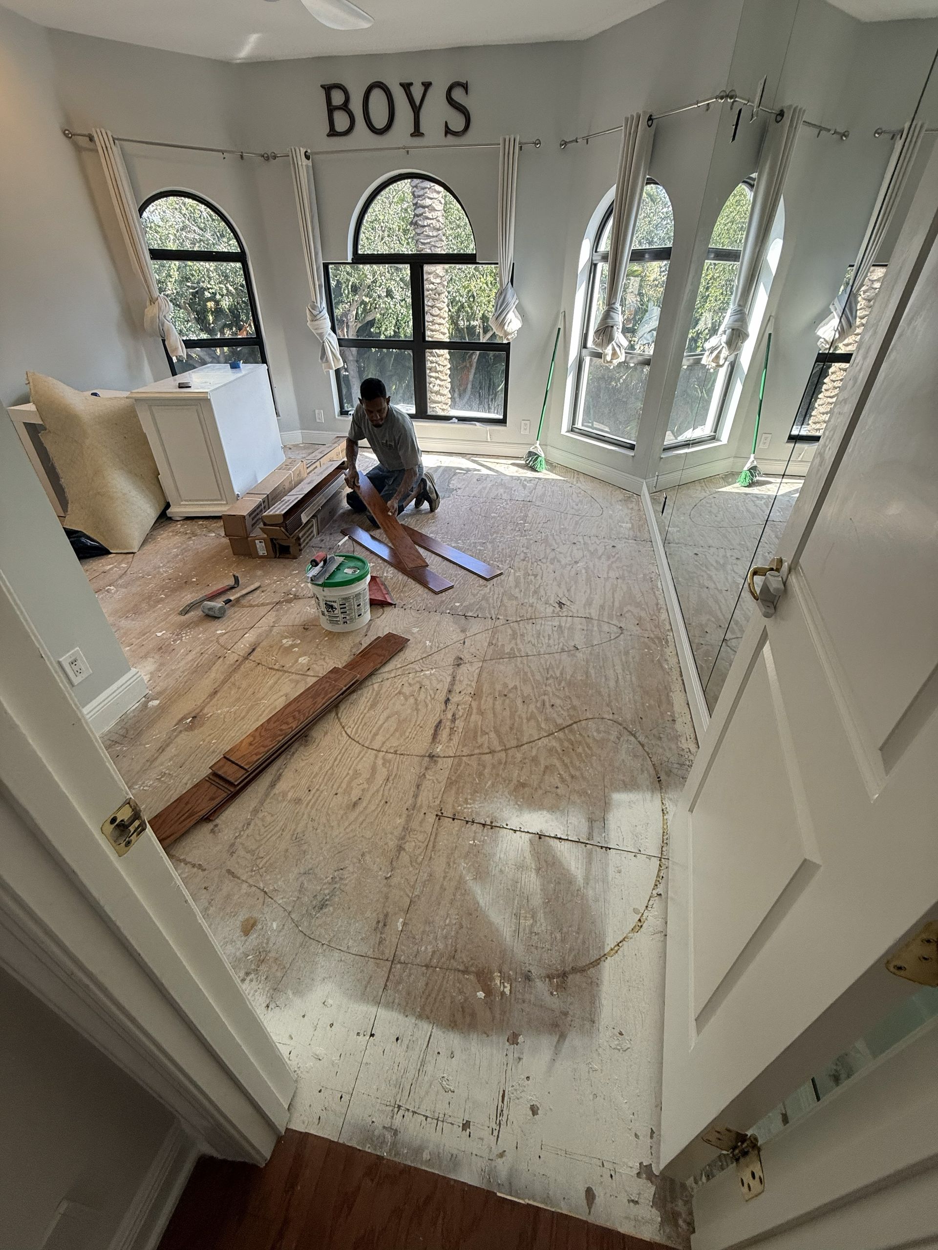 Room under renovation with person working on flooring, arched windows, and 