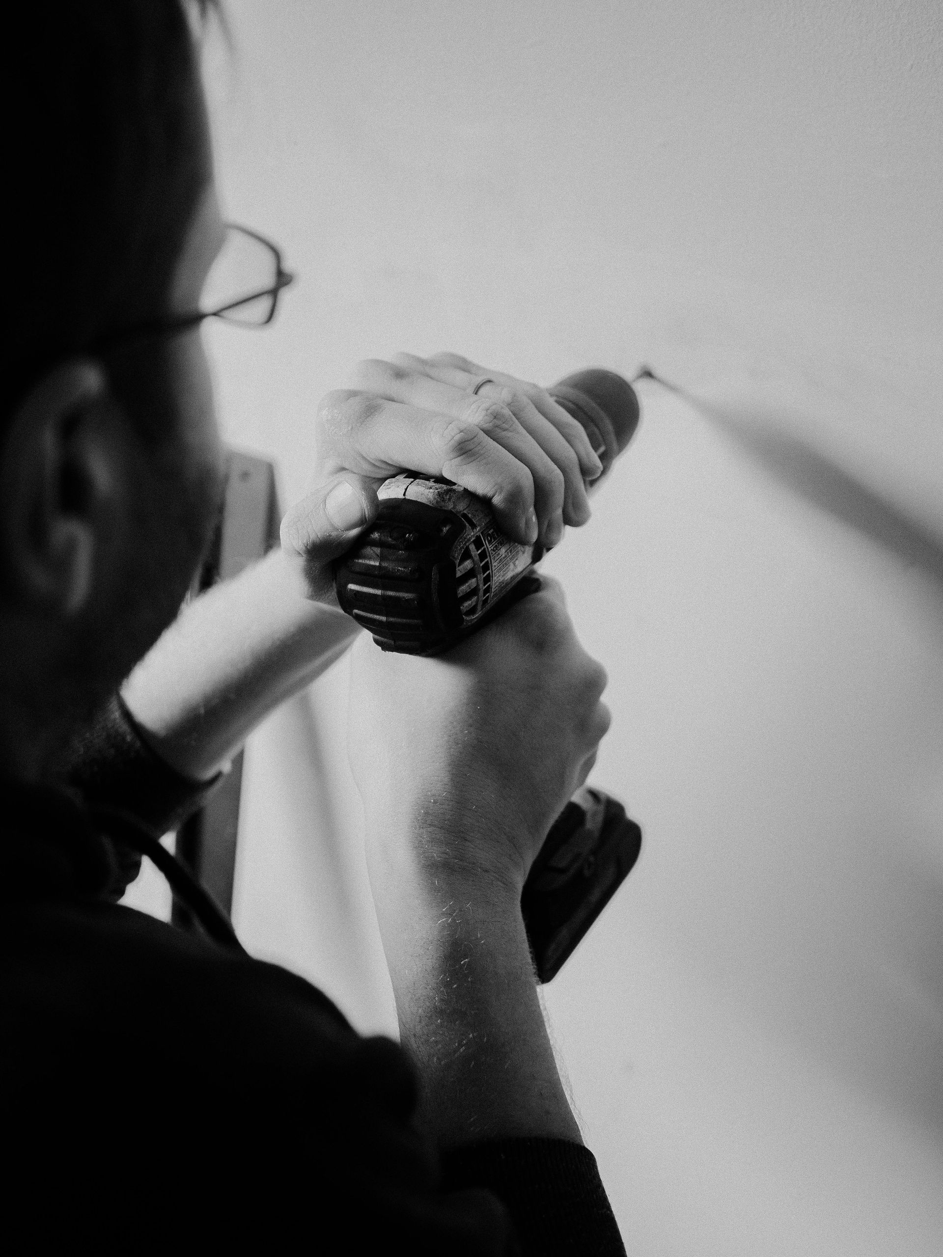 Person drilling into a white wall with a black drill.