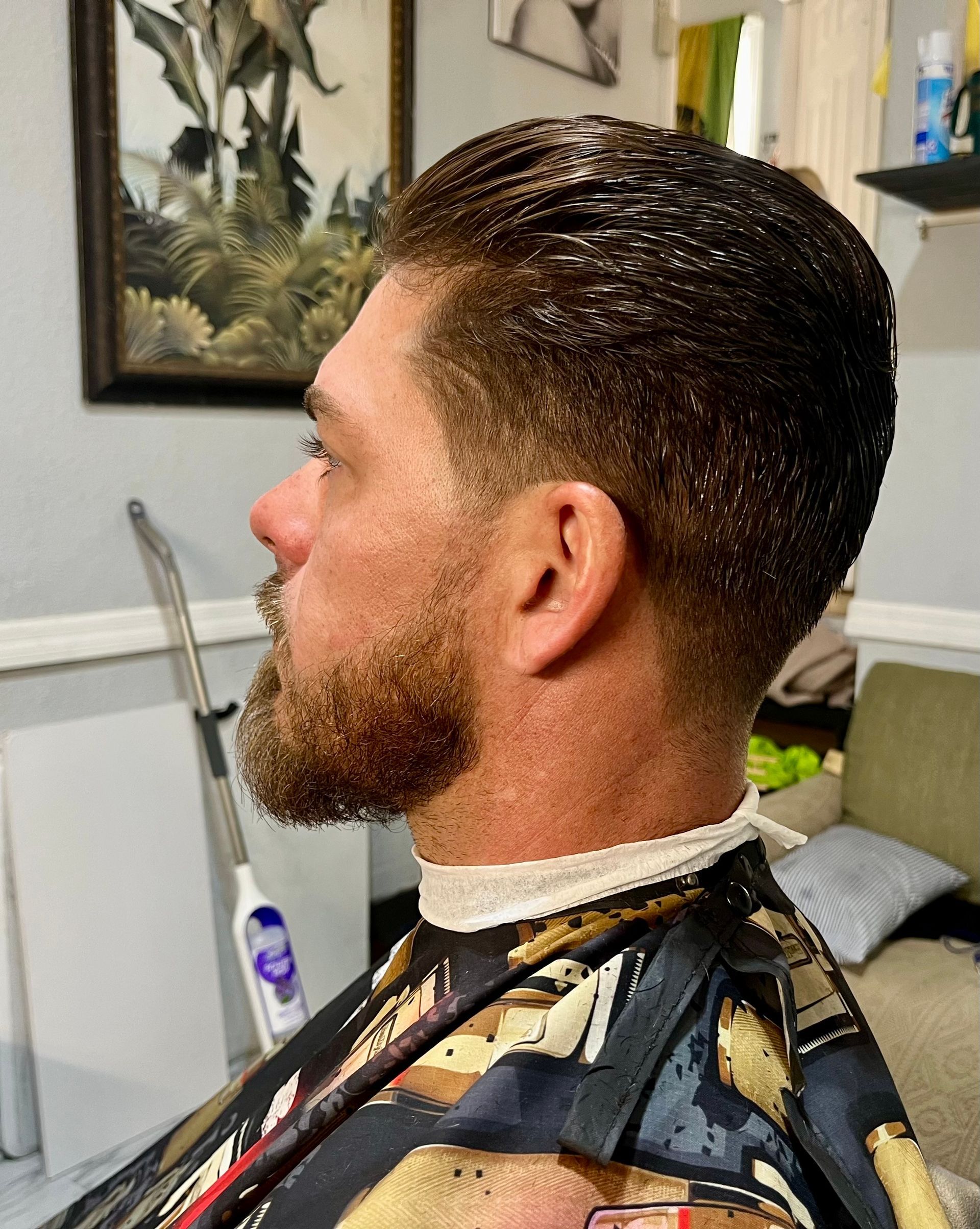 A man with a beard is getting his hair cut at a barber shop.