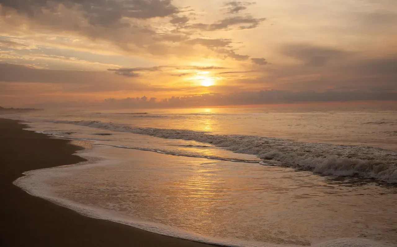 The sun is setting over the ocean and the waves are crashing on the beach.