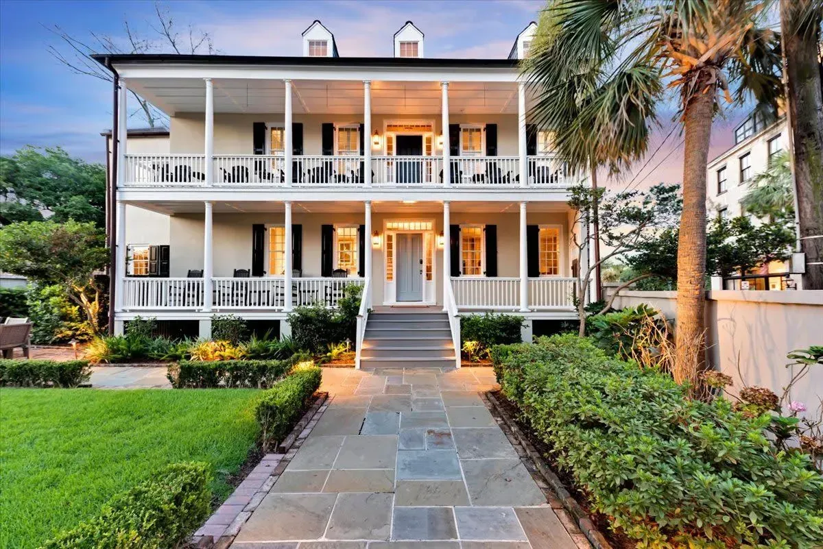 A large white house with a large porch and a stone walkway leading to it.
