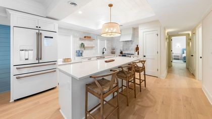 A kitchen with a large island , stools and a refrigerator.