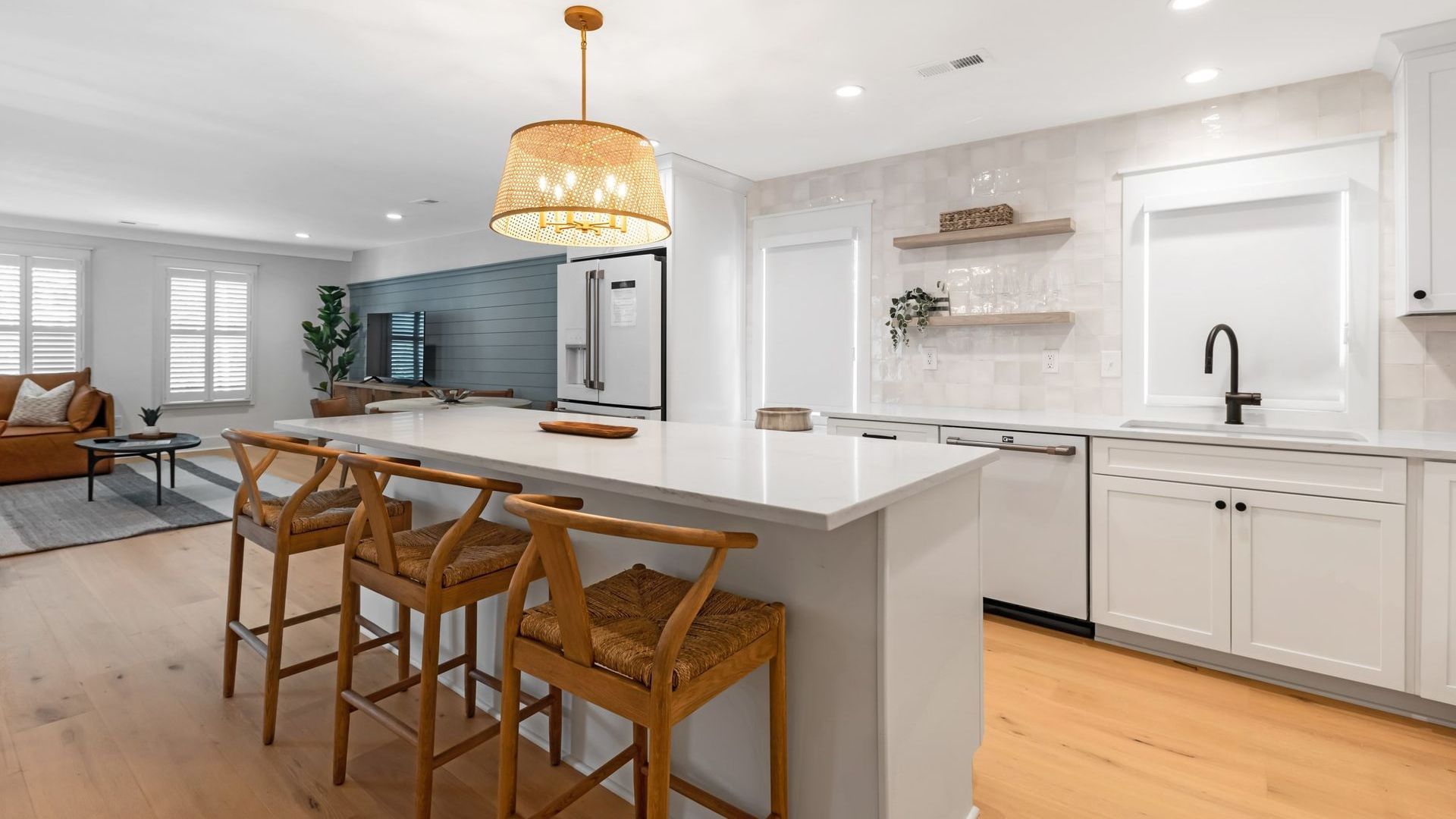 A kitchen with a large island and stools and a living room in the background.