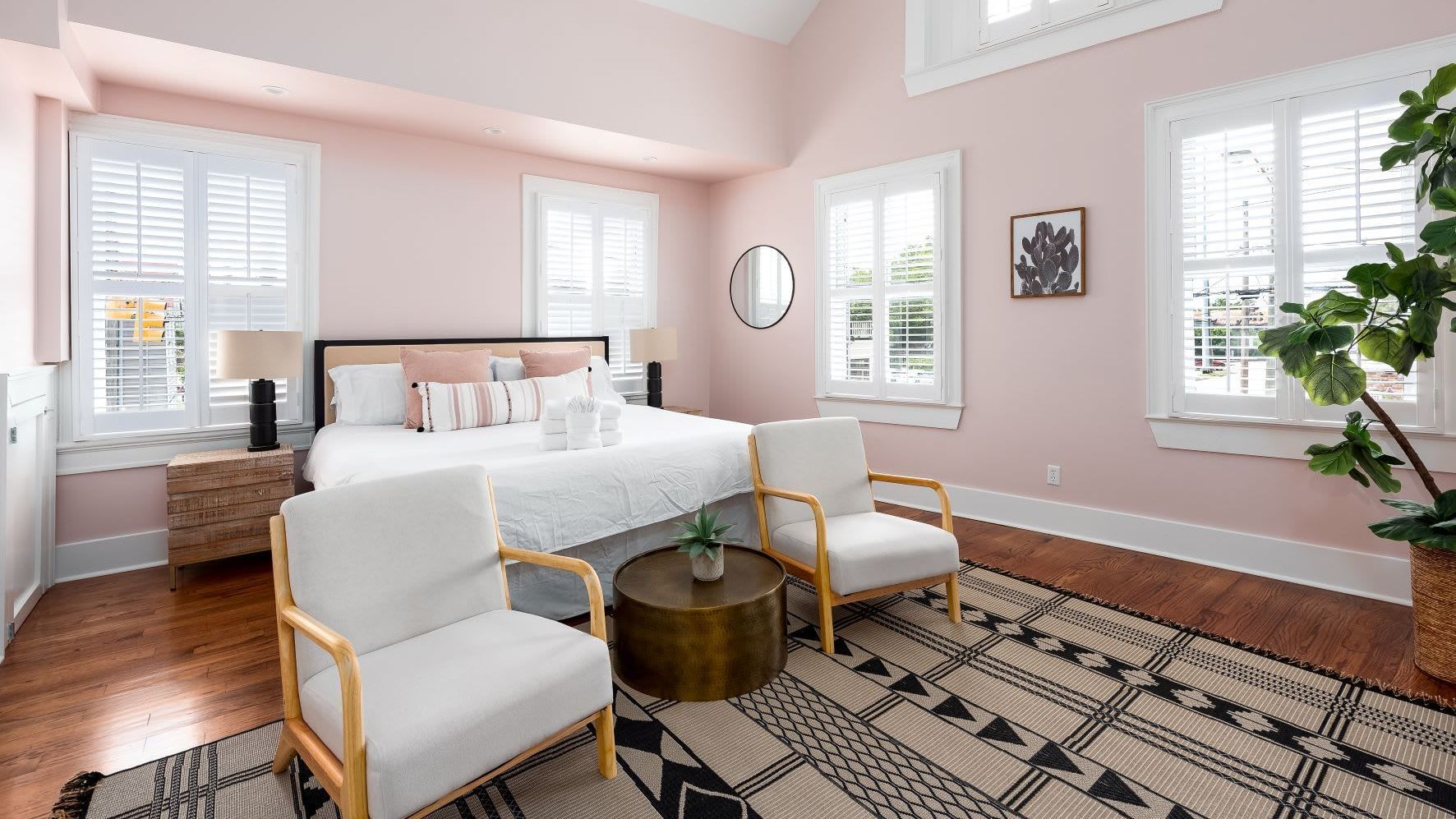 A bedroom with pink walls , a bed , two chairs , a table and a rug.