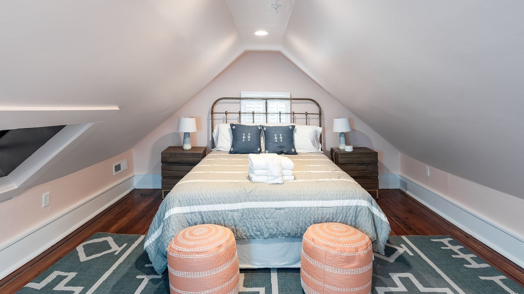 A bedroom with a bed and two ottomans in the attic.