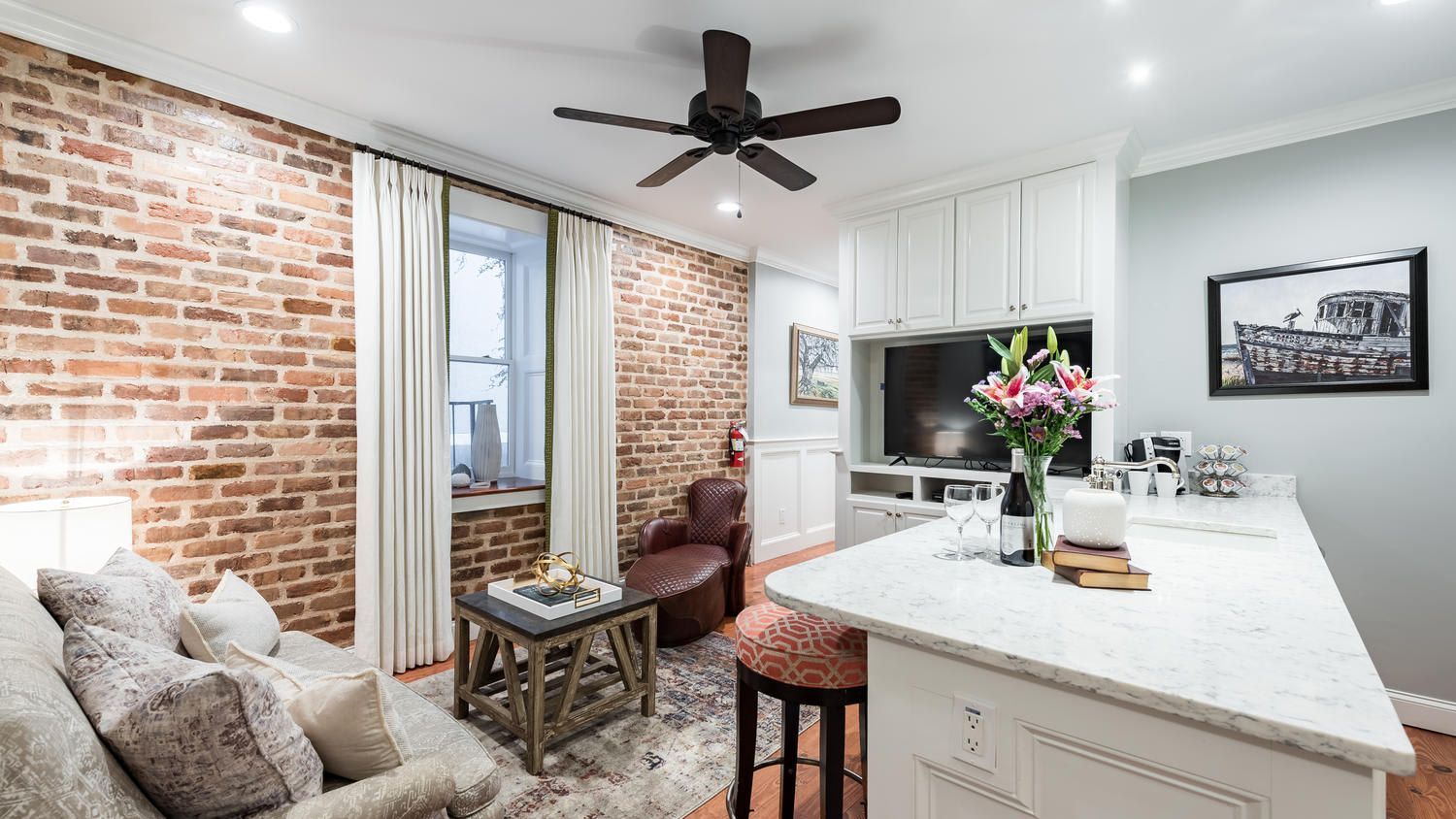 A living room with a ceiling fan and a brick wall.