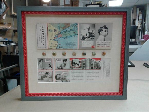 Framed display of vintage ephemera with a red and blue frame, including maps, photos, and documents.