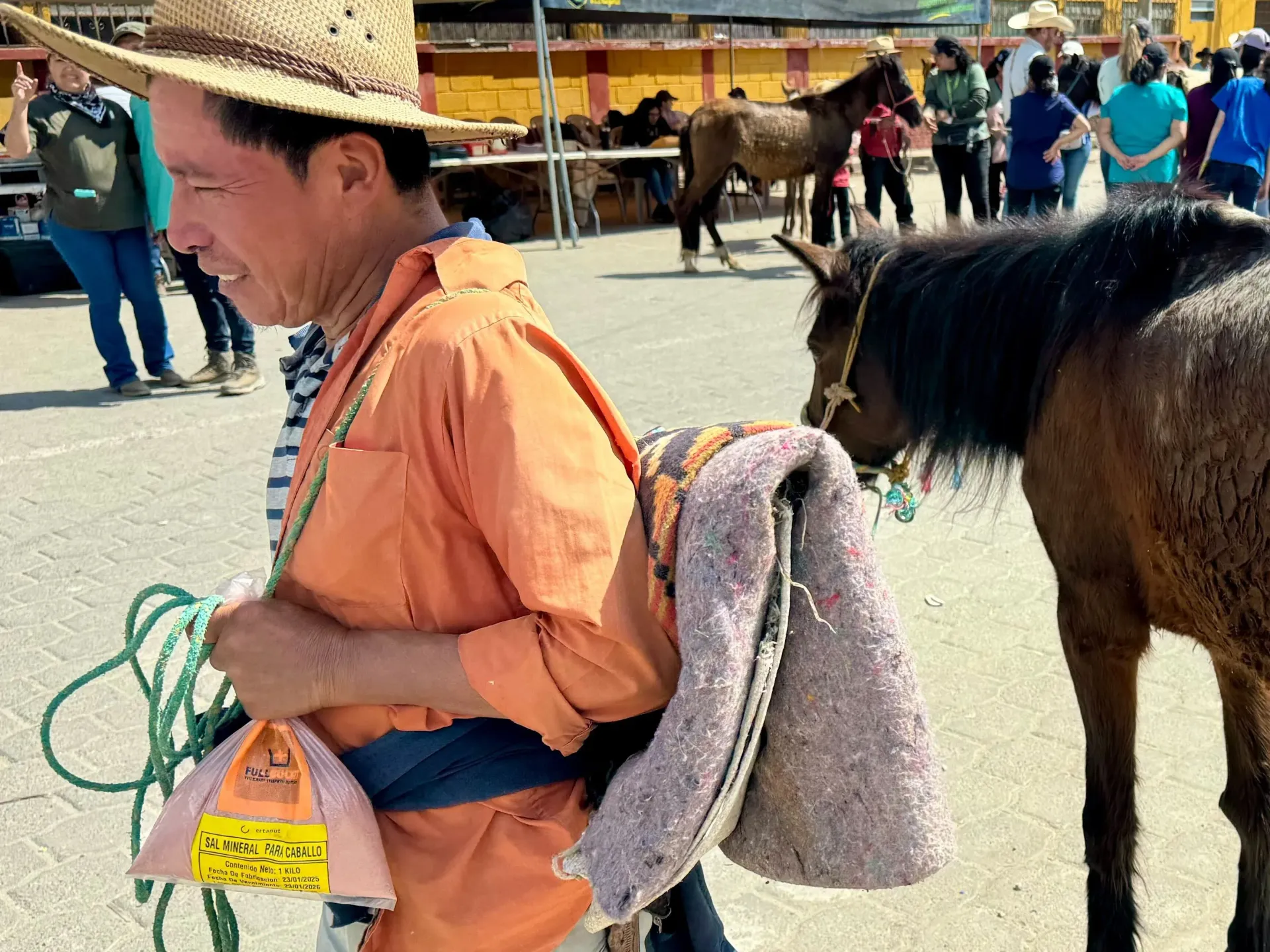 Man in orange shirt and straw hat with a horse, likely at a market.
