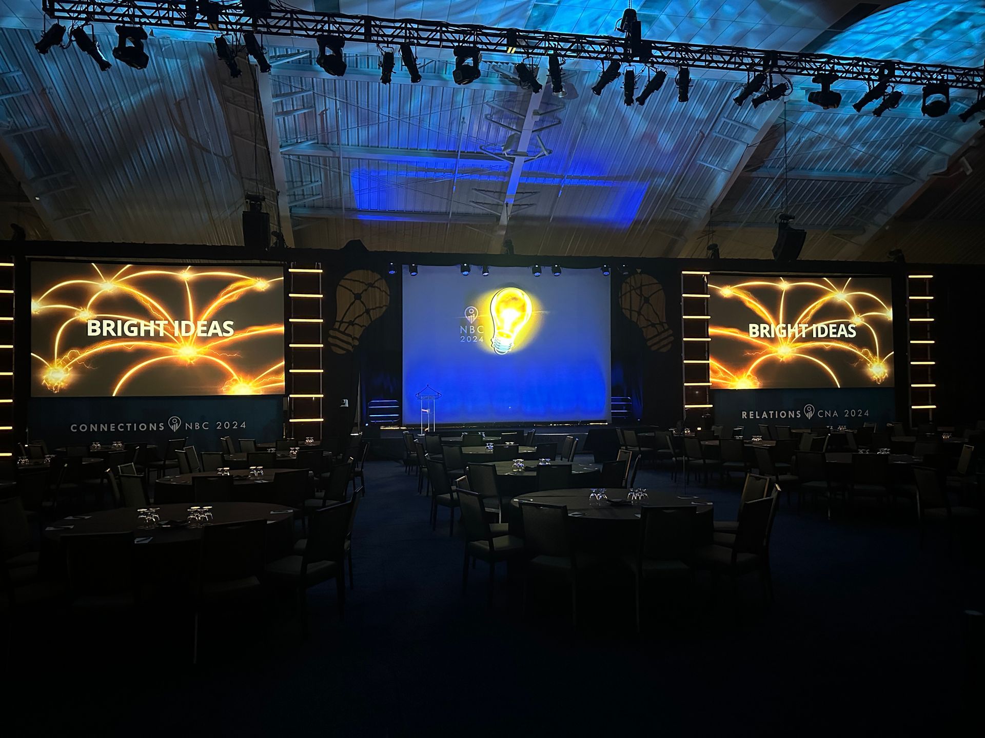 A dimly lit event hall featuring three large screens displaying 