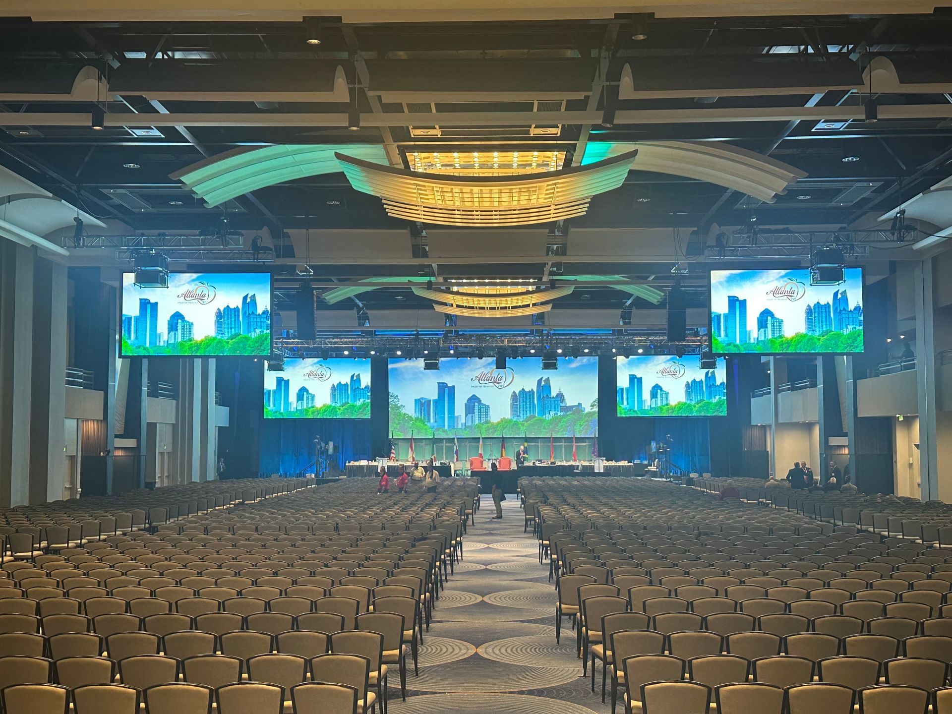 A large, empty conference room with rows of chairs facing a stage featuring screens displaying a cityscape graphic.