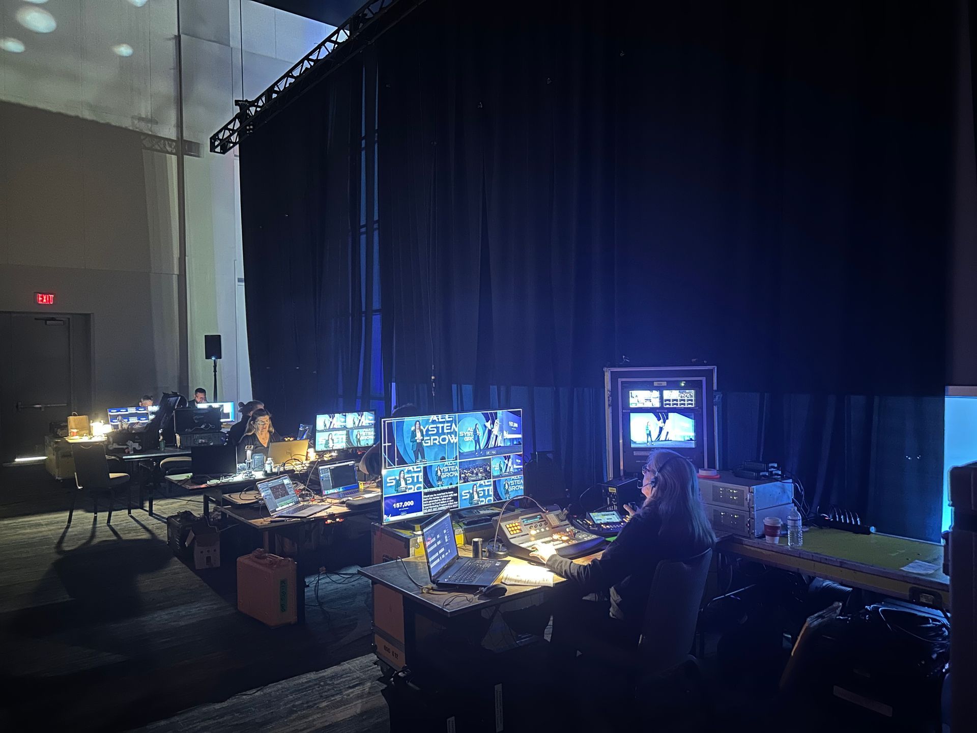 A dimly lit room with rows of people working at computer stations, managing video production equipment and monitors.