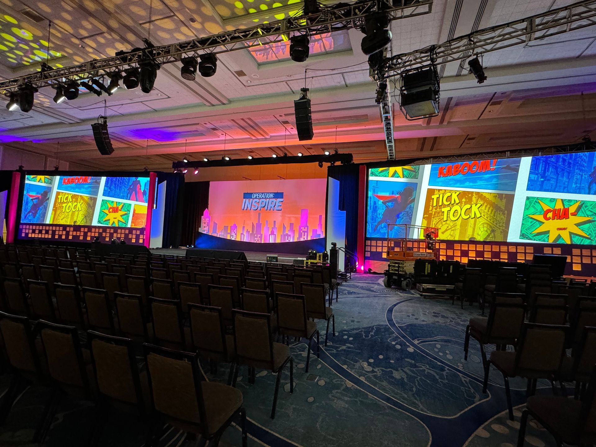 An empty conference room with rows of chairs facing a stage featuring large screens with vibrant comic-book-style art.