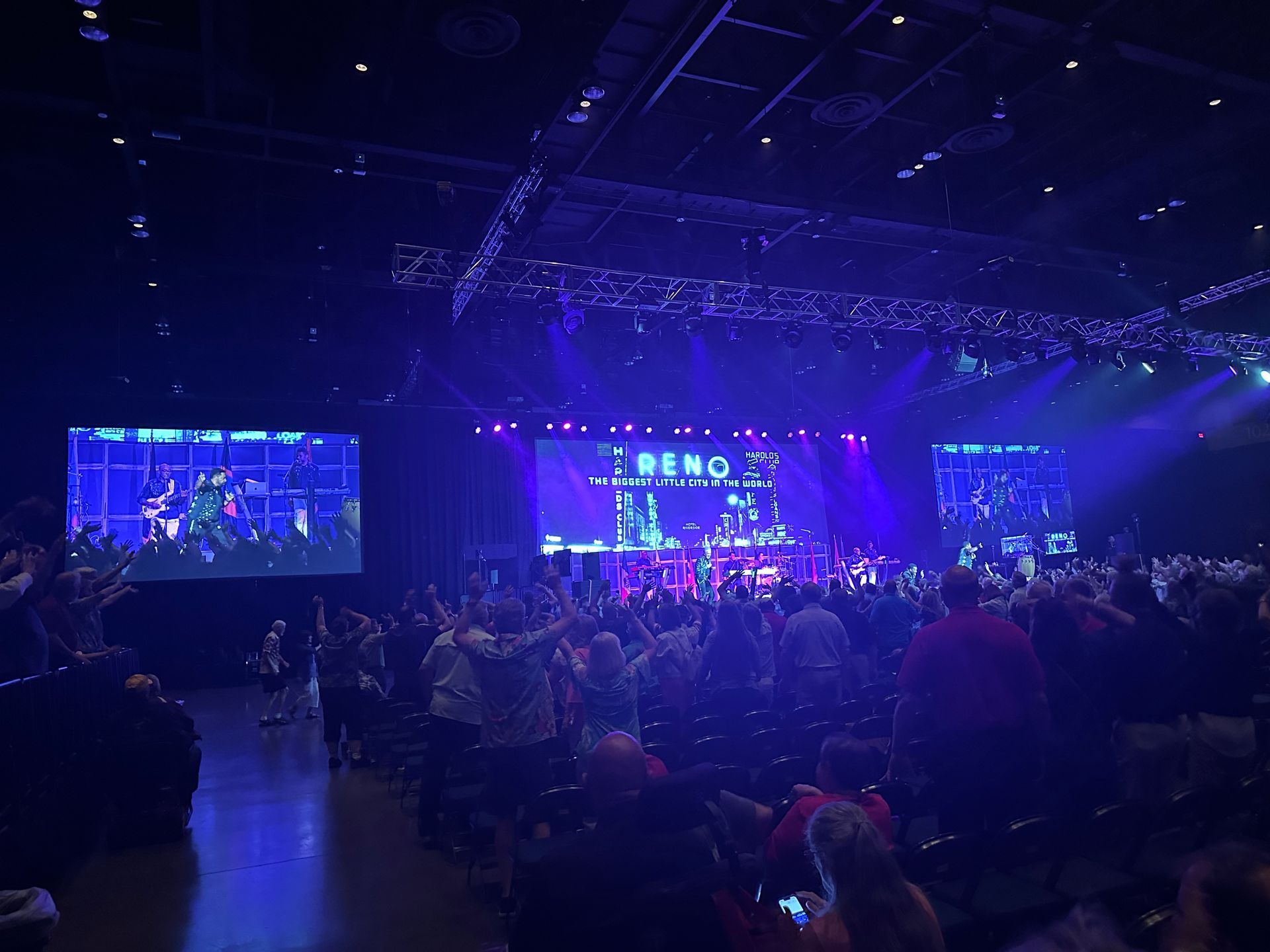 A crowd faces a stage with large screens displaying the word