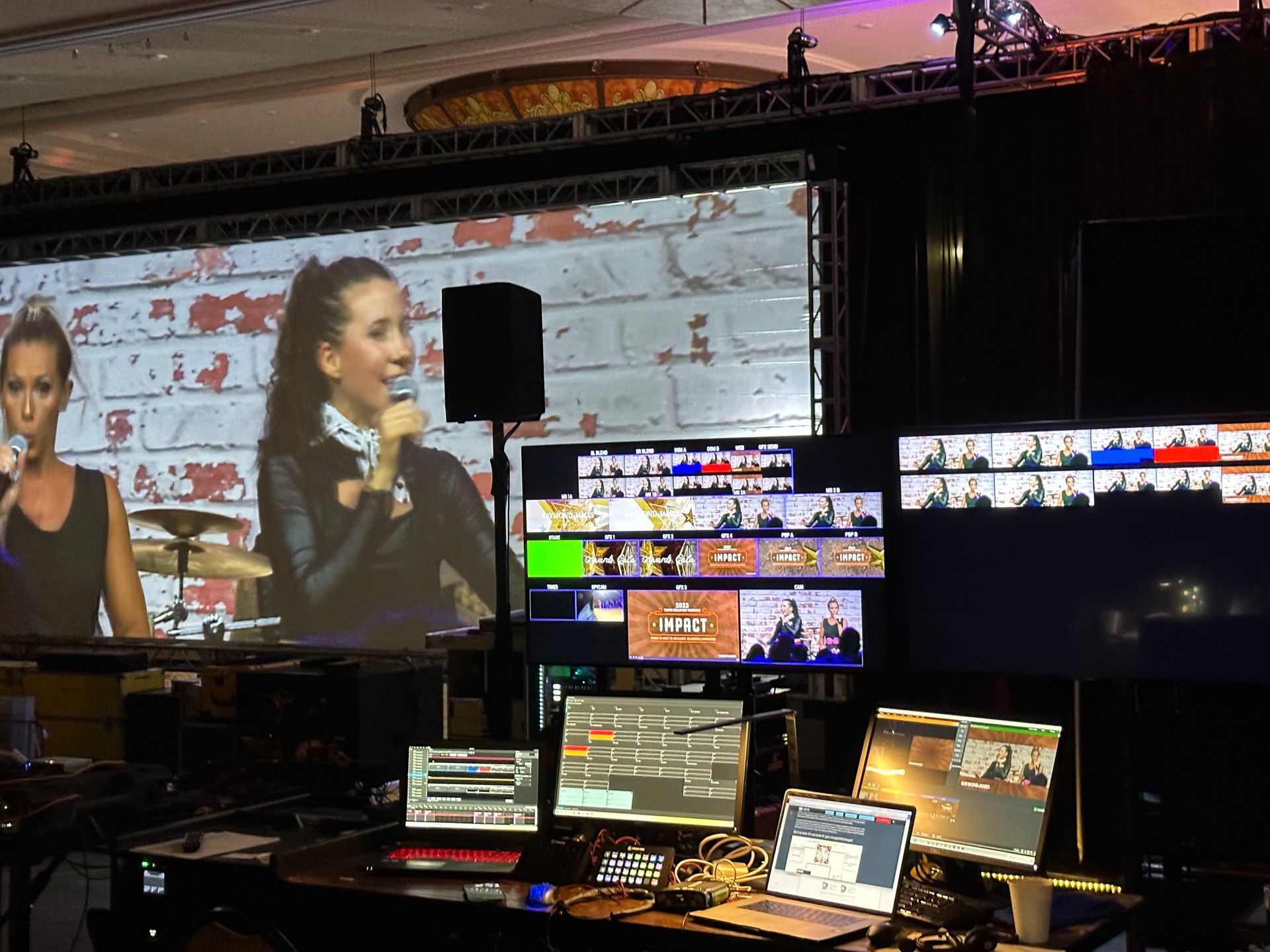 A live event control room with a large screen showing a performer and multiple monitors displaying video feeds and software.