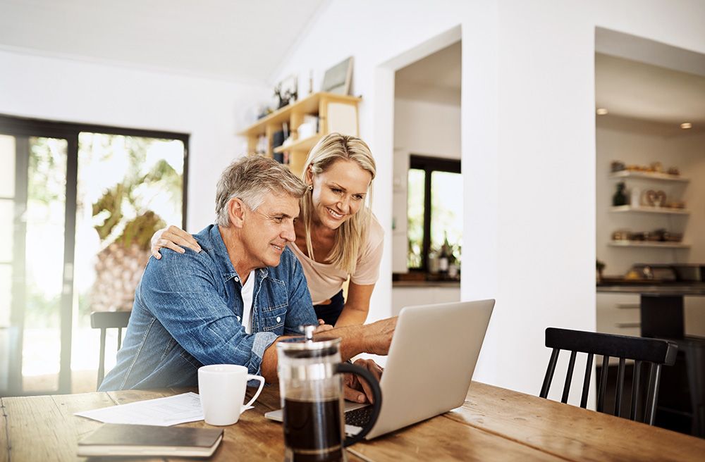 A man and a woman are sitting at a table looking at a laptop computer.