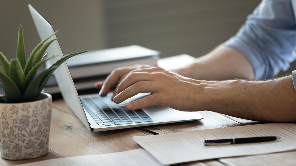 A man is typing on a laptop computer at a desk.