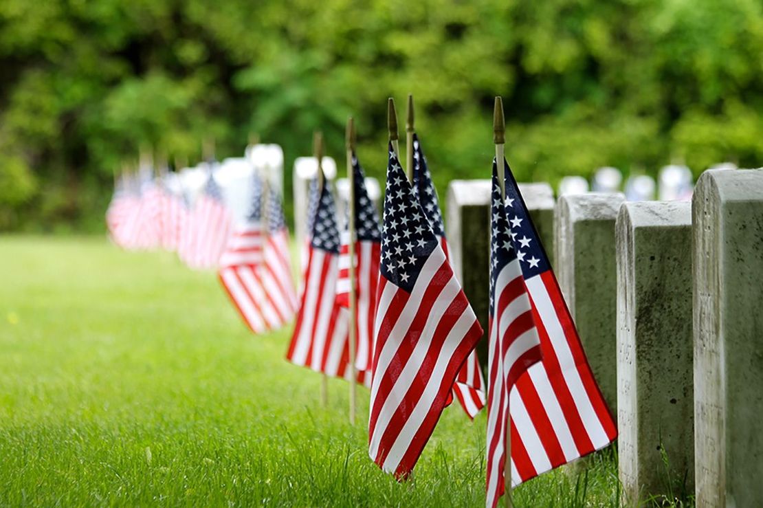 A row of american flags are lined up next to graves in a cemetery.