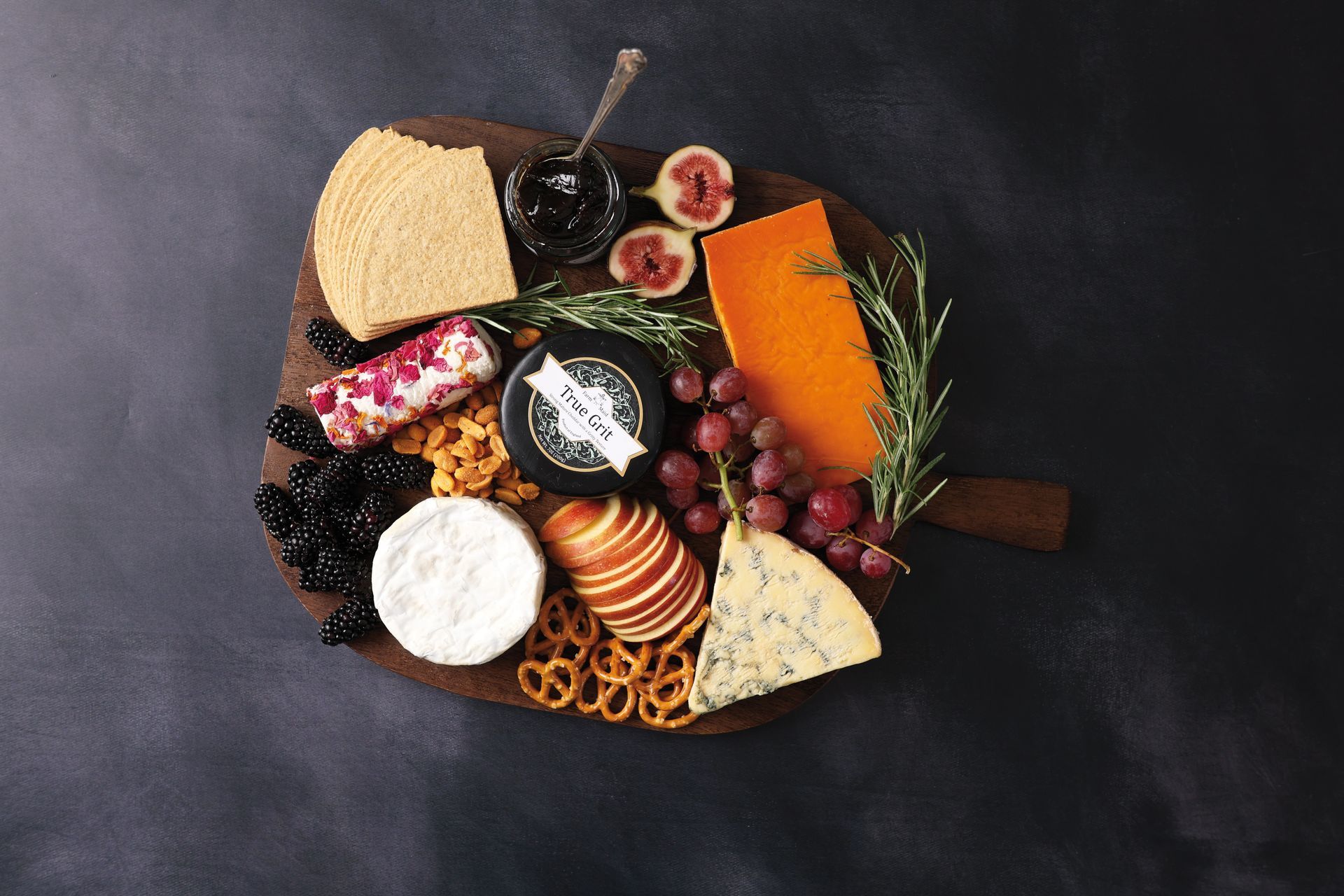 Assorted cheeses, fruit, and crackers arranged on a rustic charcuterie board