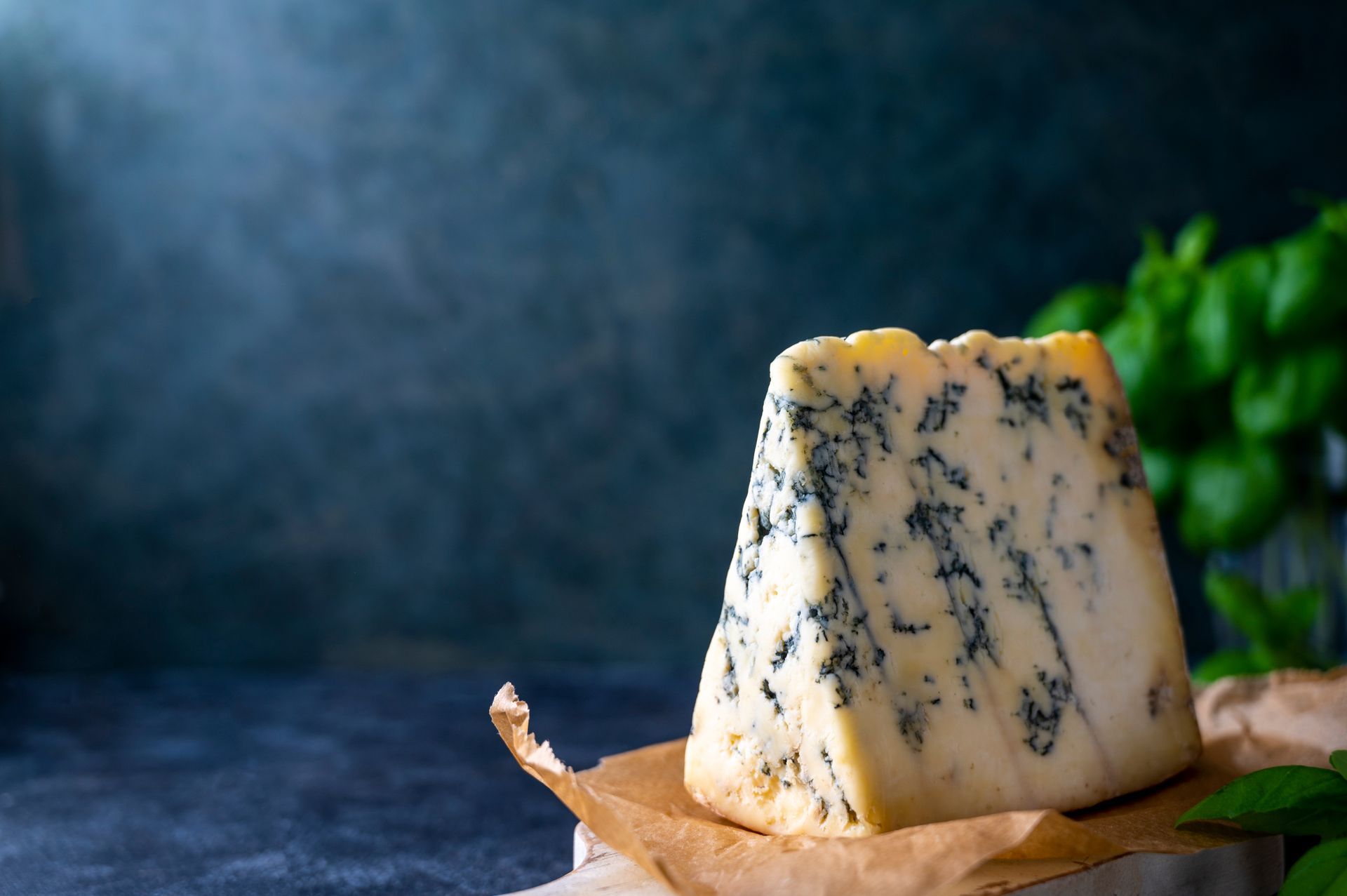 Blue-veined cheese wedge on parchment with blurred green leaves in the background