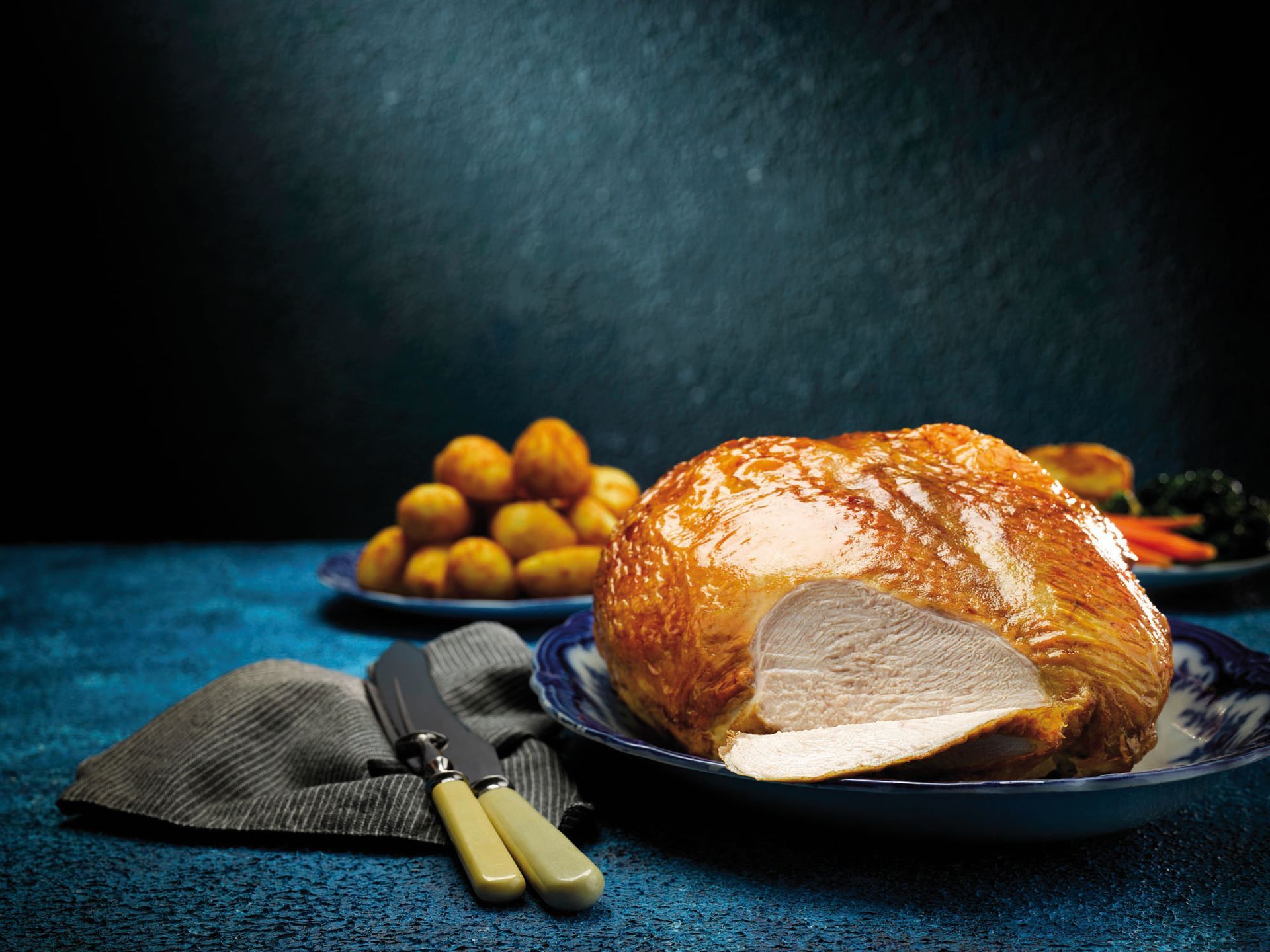 Roasted turkey on a dark plate with potatoes and a knife on a blue tablecloth