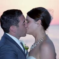 Bride and groom kissing at sunset by the water