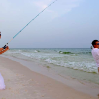 People flying a kite on a sandy beach beside small ocean waves