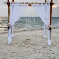 White-draped beach arch by the ocean at sunset