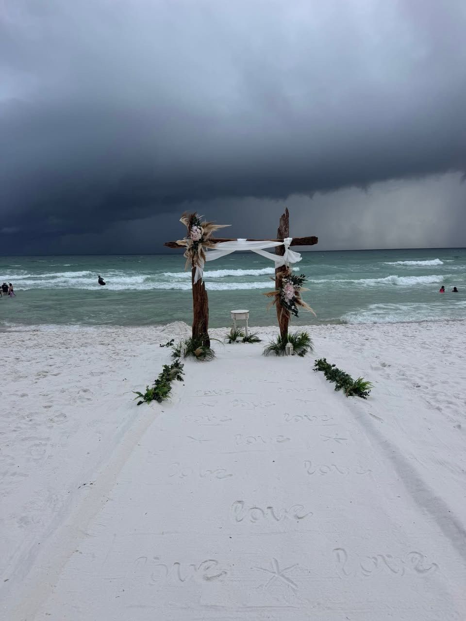 Snowy beach with two palm trunks tied together, ocean swimmers, and dark storm clouds overhead