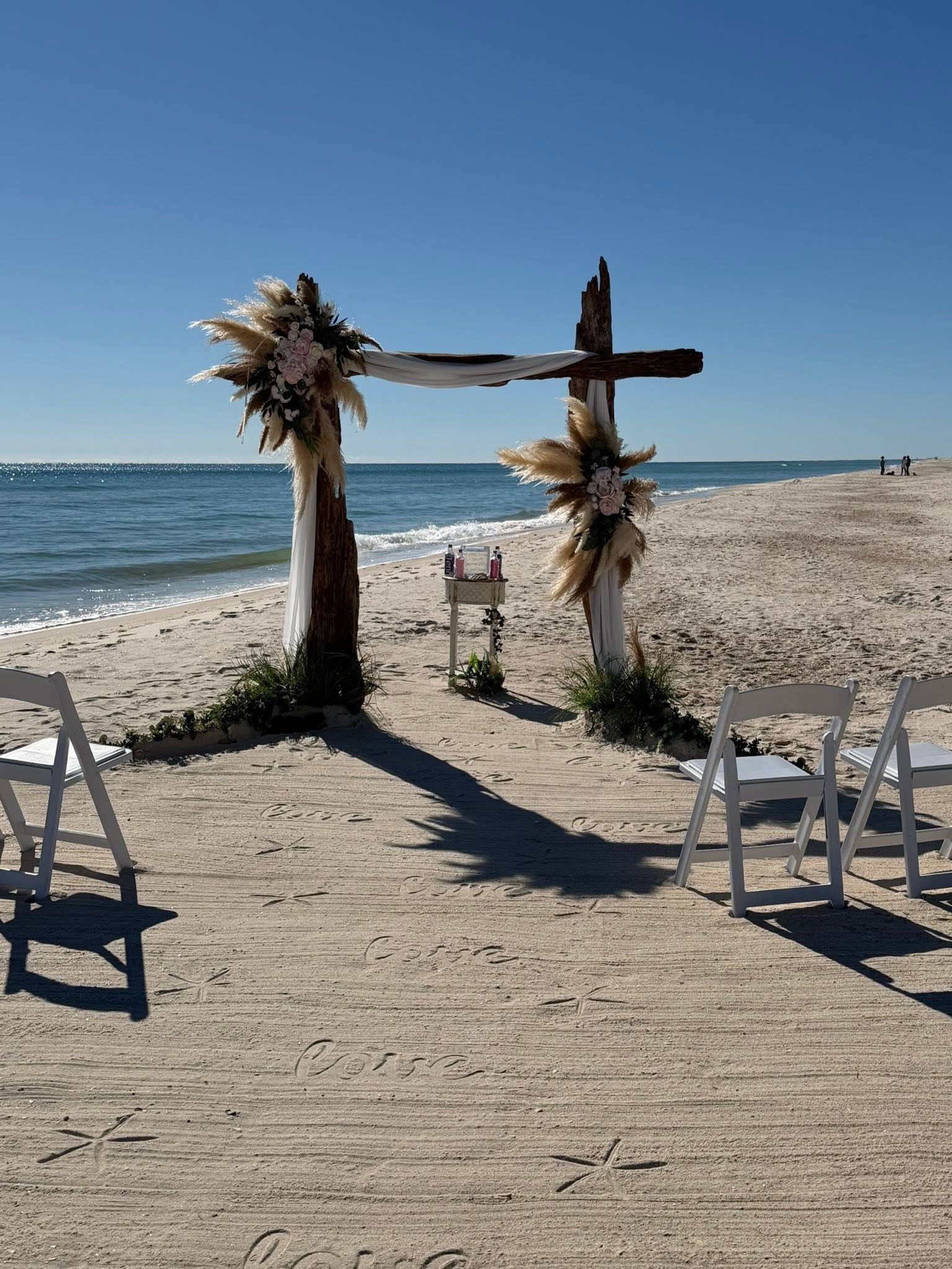 Beach wedding arch with floral decorations on a sandy shore by the ocean under a clear blue sky