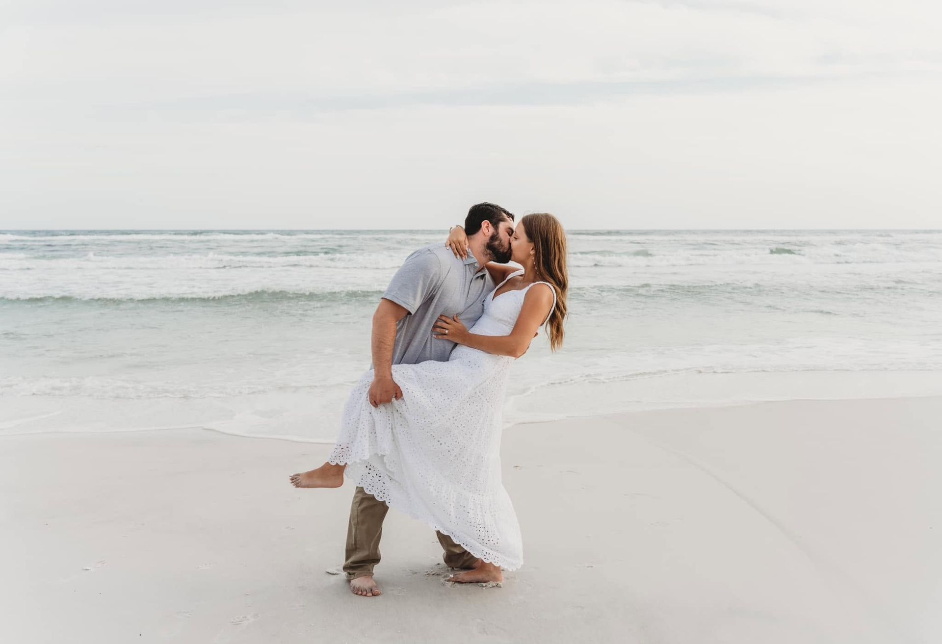 Couple kissing on a sandy beach by the ocean, with waves in the background.