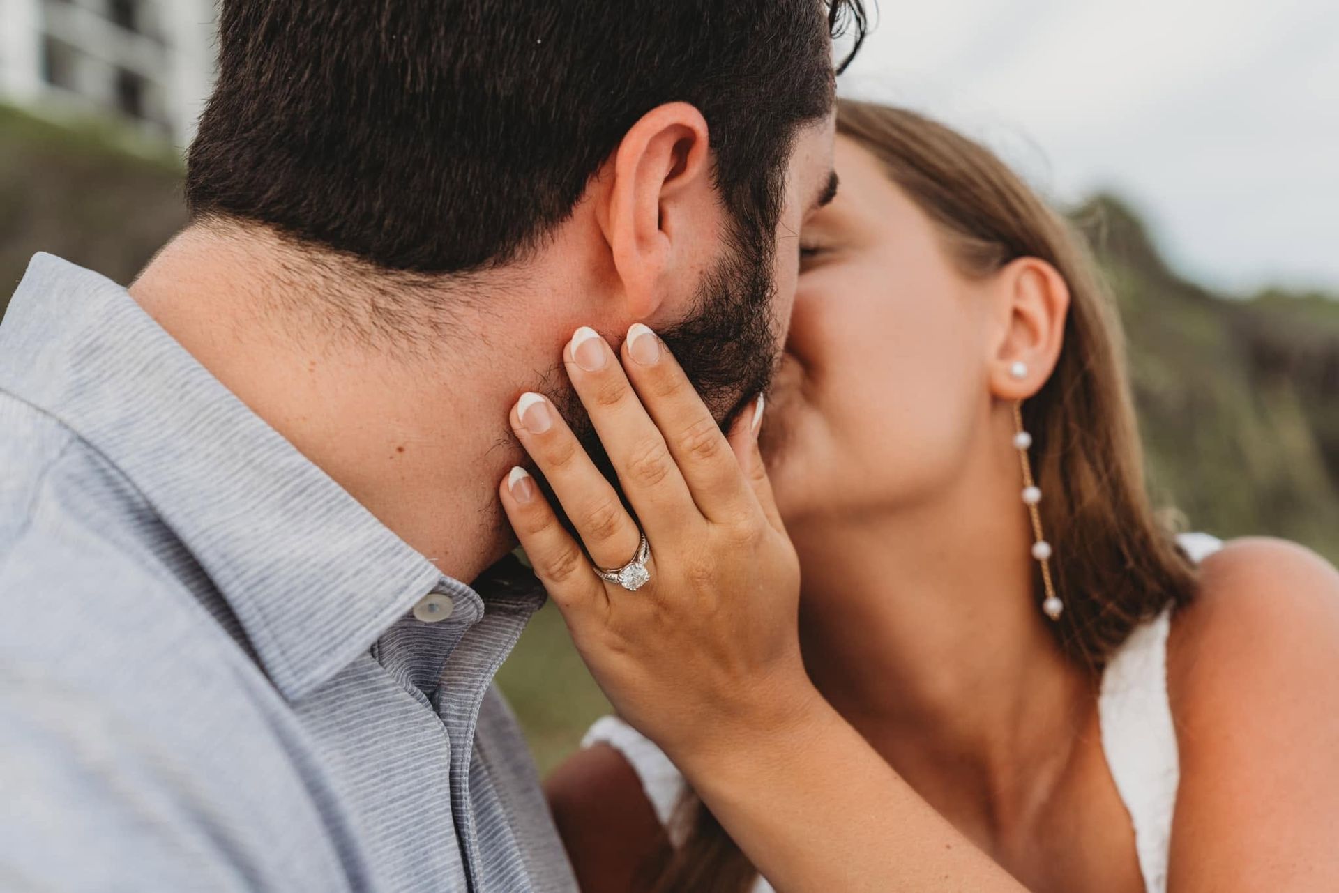 Couple kissing close-up, with a hand on the man’s cheek and an engagement ring visible