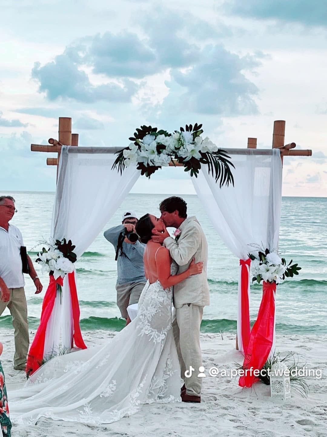 Beach wedding couple kissing under white floral arch by the sea