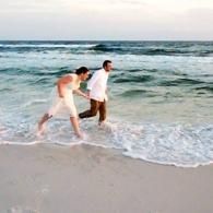Two people walking along the shoreline as waves lap at their feet at sunset