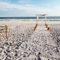 Beach wedding arch on a sandy shoreline with white fabric and red flowers by the ocean