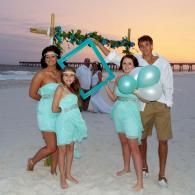 Group of people in mint outfits holding balloons on a beach at sunset