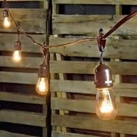 Hanging string lights with glowing bulbs against a wooden slat wall