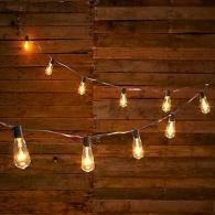 String lights hanging in front of a rustic wooden wall, glowing warmly at night.