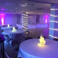 Purple-lit banquet hall with round tables, white chair covers, and glowing centerpieces