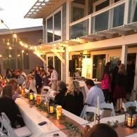 Outdoor dinner party under string lights at a long white table beside a modern house