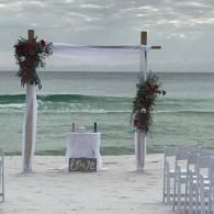 Beach wedding arch with flowers facing the ocean, with chairs and a small table on the sand