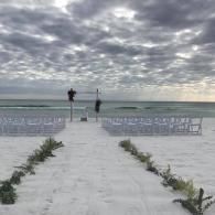 Beach wedding aisle with white chairs facing the ocean under a cloudy sky