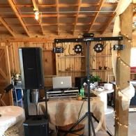 Indoor rustic room with stage lights, speaker, laptop, and equipment on stands among tables and chairs