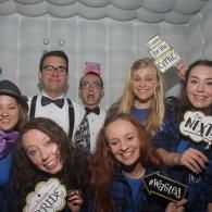 Group posing at a party, smiling with playful photo props under a white tent.
