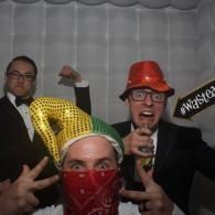 Four people posing at a party in colorful hats and masks, smiling in front of a photo booth backdrop