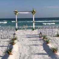 Beach wedding aisle with white chairs and floral arch facing the ocean